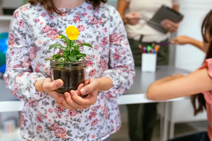 Female student holding a pansy plant on her hands in ecology classroom