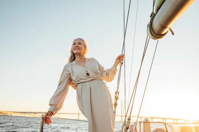 Older happy woman standing on a boat at sunset