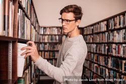 Male college student picking book from library wall 5loR60
