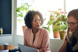 Two female business woman working together in a bright office with plants