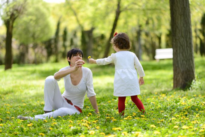 Woman with daughter playing with flowers in sunny park