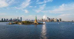 Aerial Helicopter Cinematic Passing View of the Statue of Liberty with Manhattan Skyline Cityscape. Panoramic View of New York City Skyscrapers and Jersey City Buildings on a Sunny Day