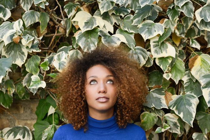 Woman with curly hair looking up in front of wall of leaves