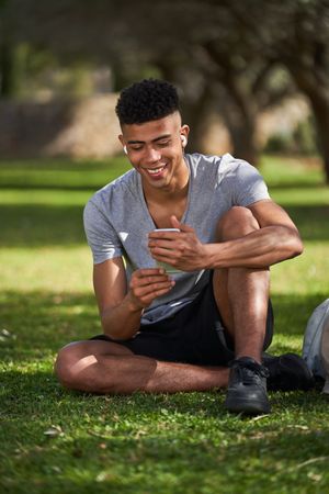 Cheerful male using smartphone for listening music on green lawn