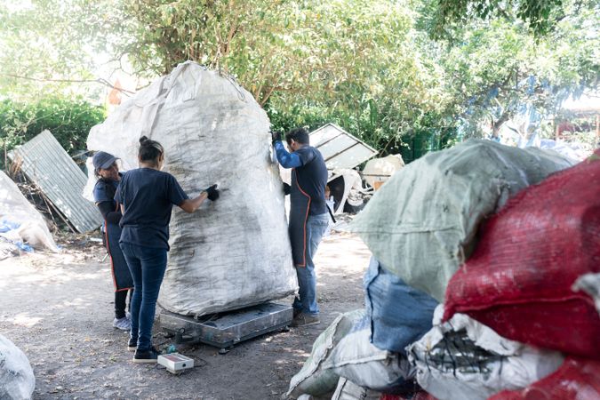 Young Hispanic Workers Weighing a Huge Sack of Recycled Plastic