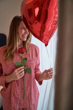 Happy woman with rose and red heart balloon at window