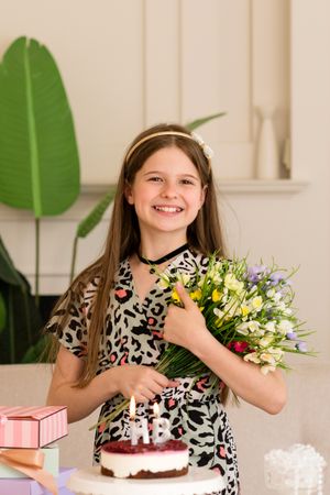 Girl holding bouquet of flowers next to birthday cake.