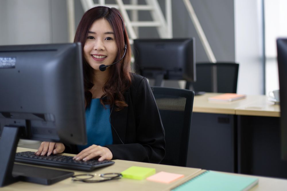 Asian woman staff at service desk talking on phone in a call centre