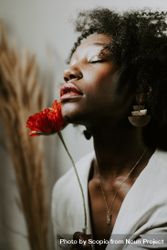 Woman with curly hair smelling red flower 5awlab