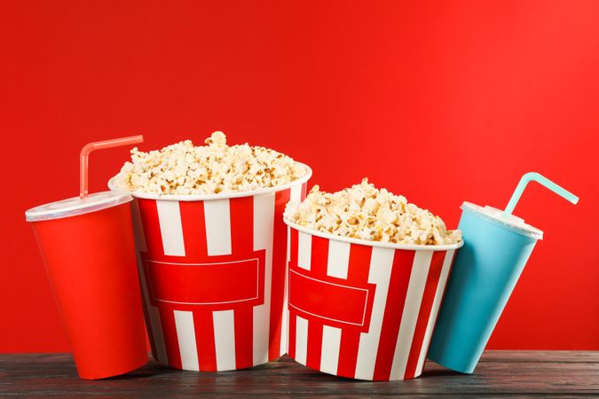 Popcorn buckets and paper cups against red background, space for text
