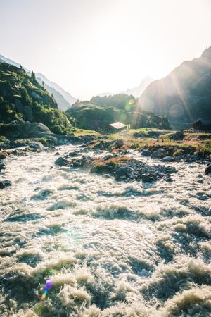 Foamy mountain stream flowing through stones in sunlight