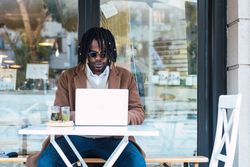 Black man browsing on laptop on restaurant terrace