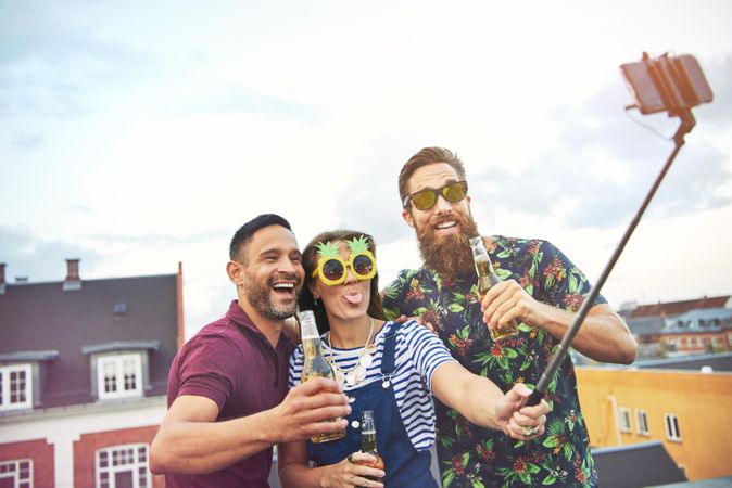 Three friends with beer an pineapple glasses taking a selfie on a roof