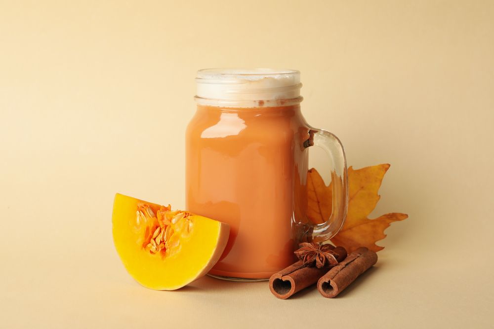 Composition with pumpkin latte, pumpkin, leaf and cinnamon on beige background