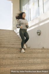 Woman running down concrete stairs outside in an urban setting 0JGZd5