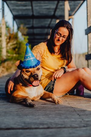 Casual young woman resting next to brown dog with party hat
