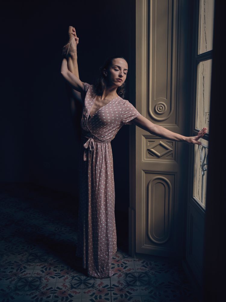 Woman in pointe with raised leg in dim light