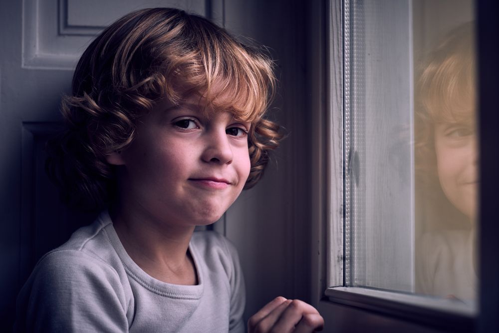 Adorable little boy smiling at camera near window