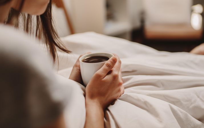 Close up of a woman sitting on bed holding a cup of coffee