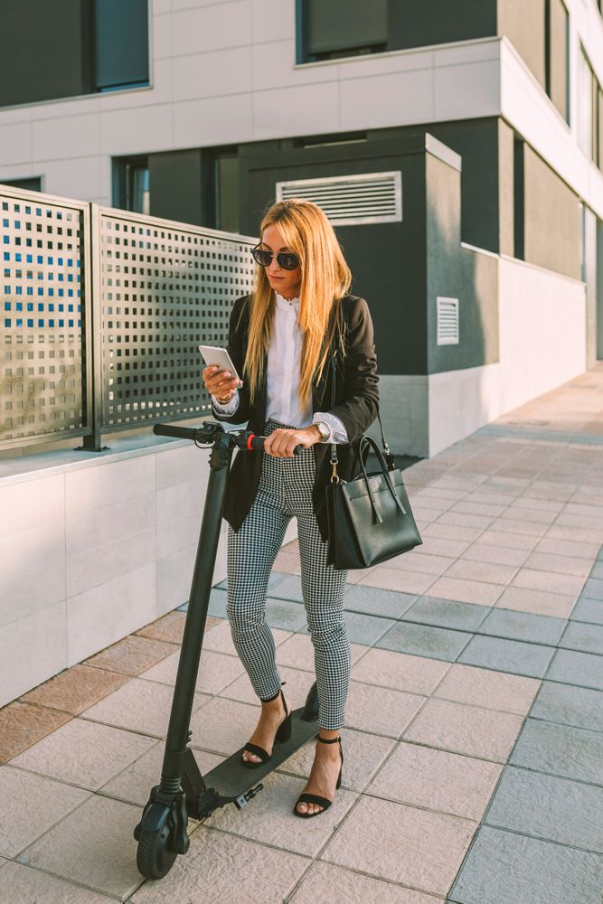 Businesswoman with e-scooter looking at cellphone