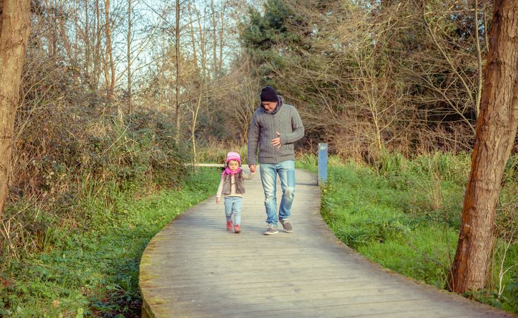 Father and young daughter walking along trail in forest