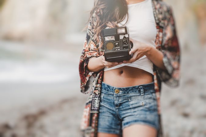 Woman with camera on shore near stones and water