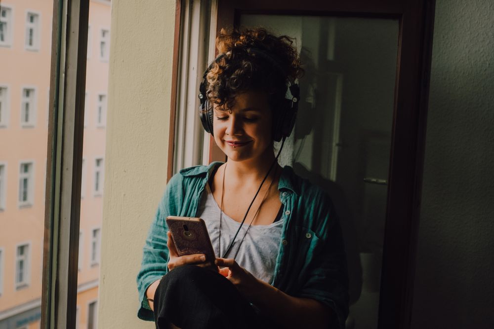 Cheerful woman in headphones using smartphone at home