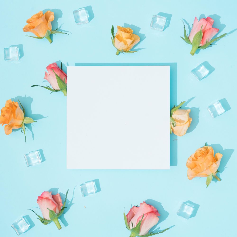 Pattern made of colorful flowers and ice cubes on pastel blue background with paper card note