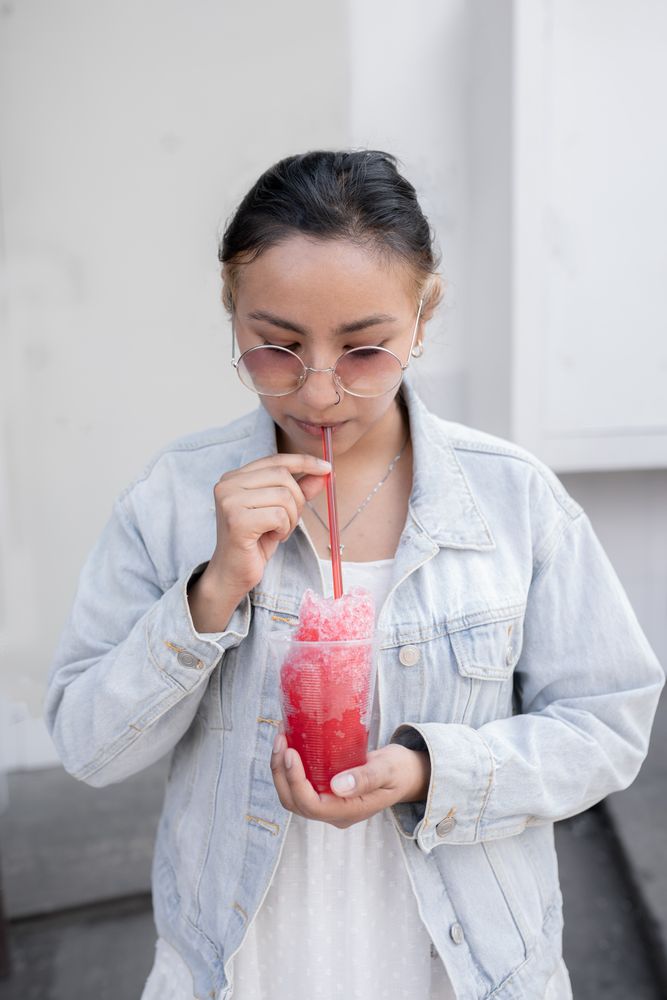 A young Hispanic woman is drinking a Mexican cherry slushy using a straw