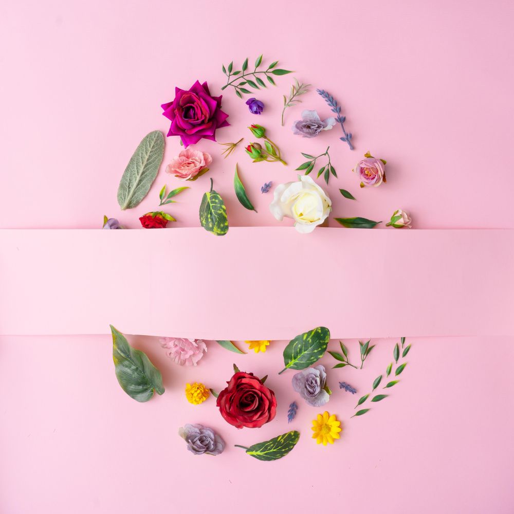 Easter egg shape made with various spring flowers and leaves on pastel pink background