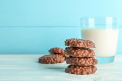Stack of chocolate cookies with glass of milk on table against color background