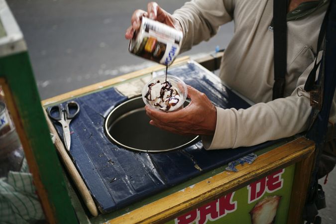 Indonesian street vendor putting chocolate sauce on ice cream