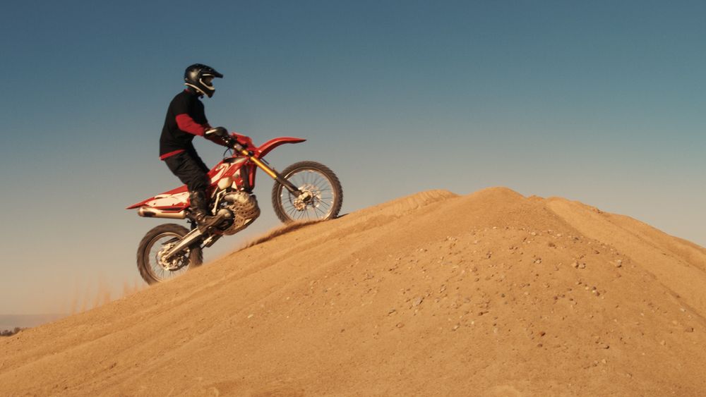 Shot of the Professional Motocross Motorcycle Rider Drives Over the Dune and Further Down the Off-Road Track.