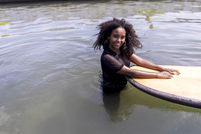 Smiling Black woman in the water next to paddle board