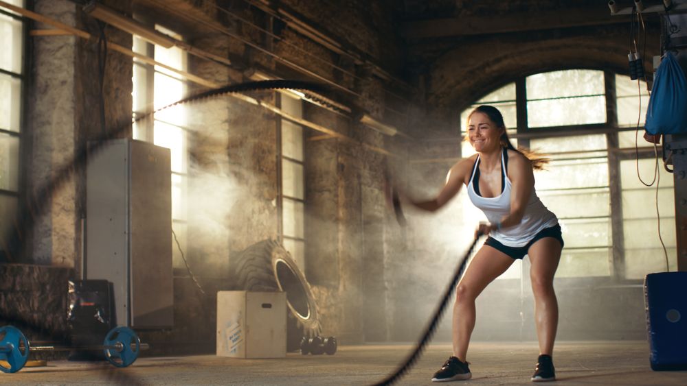 Athletic Female in a Gym Exercises with Battle Ropes During Her Cross Fitness Workout  High-Intensity Interval Training.