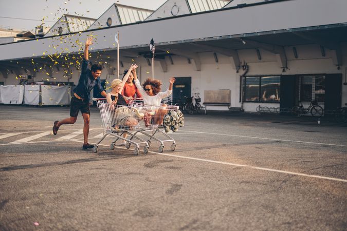 Young friends having fun on shopping trolleys and throwing confetti