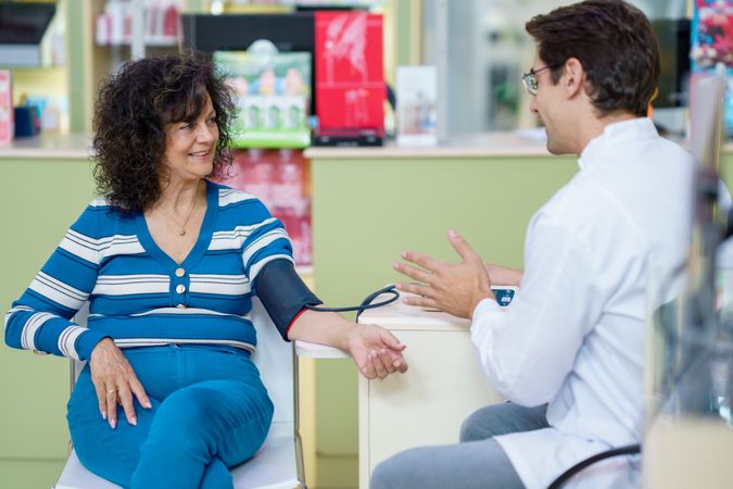 Chemist talking with client before measuring blood pressure in pharmacy
