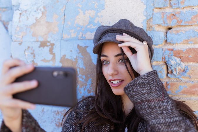Charming Hispanic lady taking selfie near wall