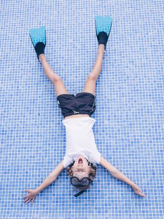 Adorable boy in snorkeling mask and flippers lying on pool