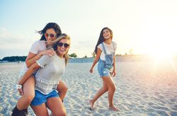 Three happy friends having fun walking on sand at the beach