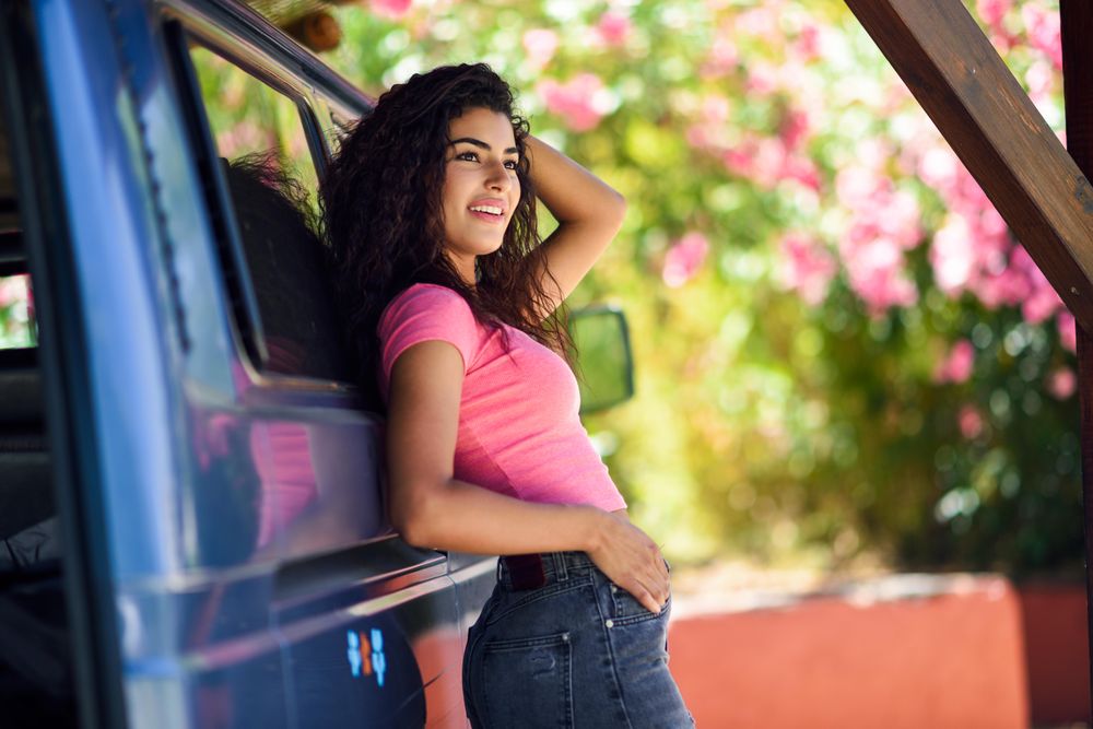 Female in pink t-shirt leaning on door to blue van with one arm to her head