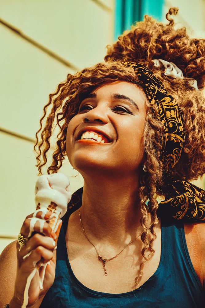 Vertical shot of smiling Black female smiling with an ice cream cone in the sun