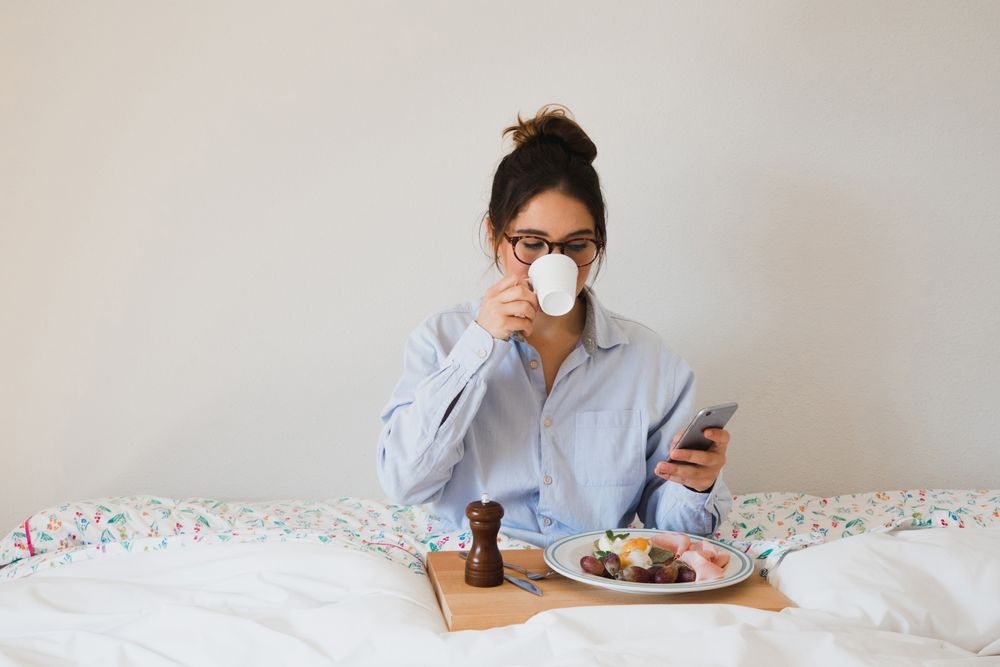 Young woman with breakfast on bed using smart phone