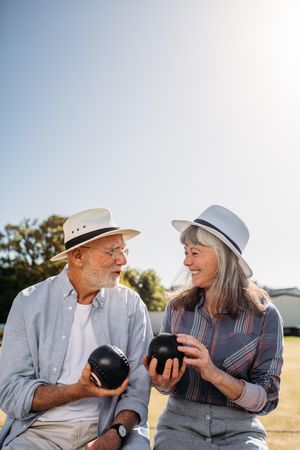 Smiling man and woman sitting together in a park and talking holding boules