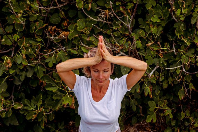 Adult woman meditating near bush