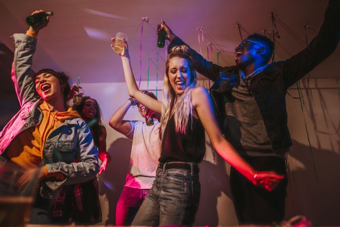 Friends dancing in joy holding drinks at a house party