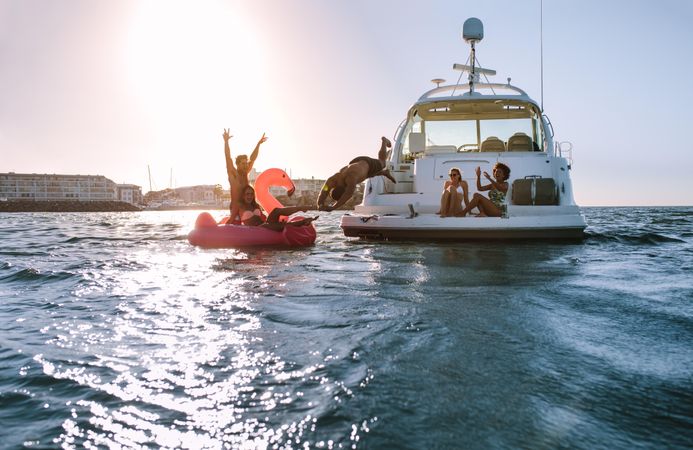 Group of friends enjoying summer day on inflatable toy and yacht