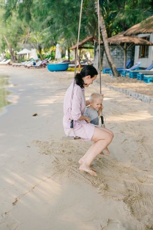 Joyful kid swinging with mother against blurred seascape