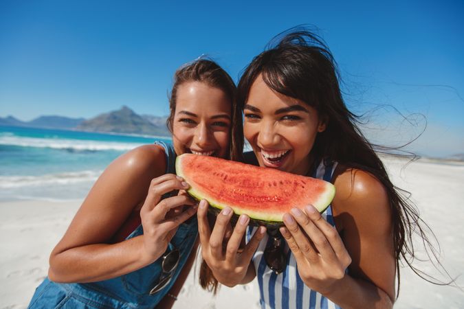 Two female models posing with watermelon slice at the beach