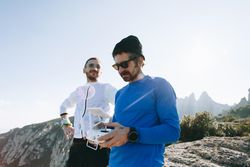Two men on hill, one holding remote